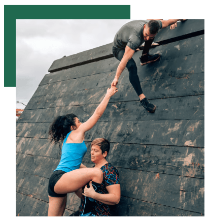 Teamwork in action as one person helps another climb a wooden obstacle.