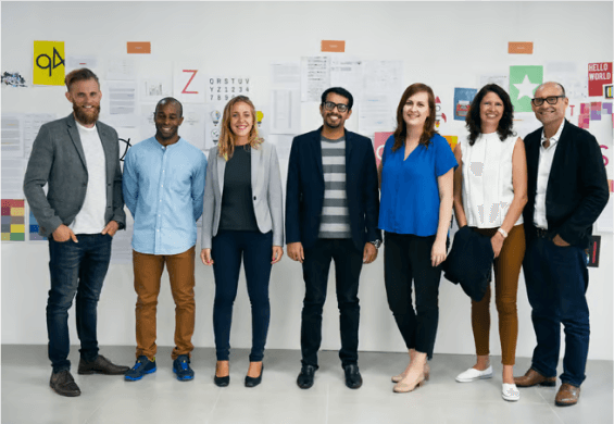 A diverse team of professionals stands confidently in front of a creative workspace, showcasing collaboration, expertise, and innovation.